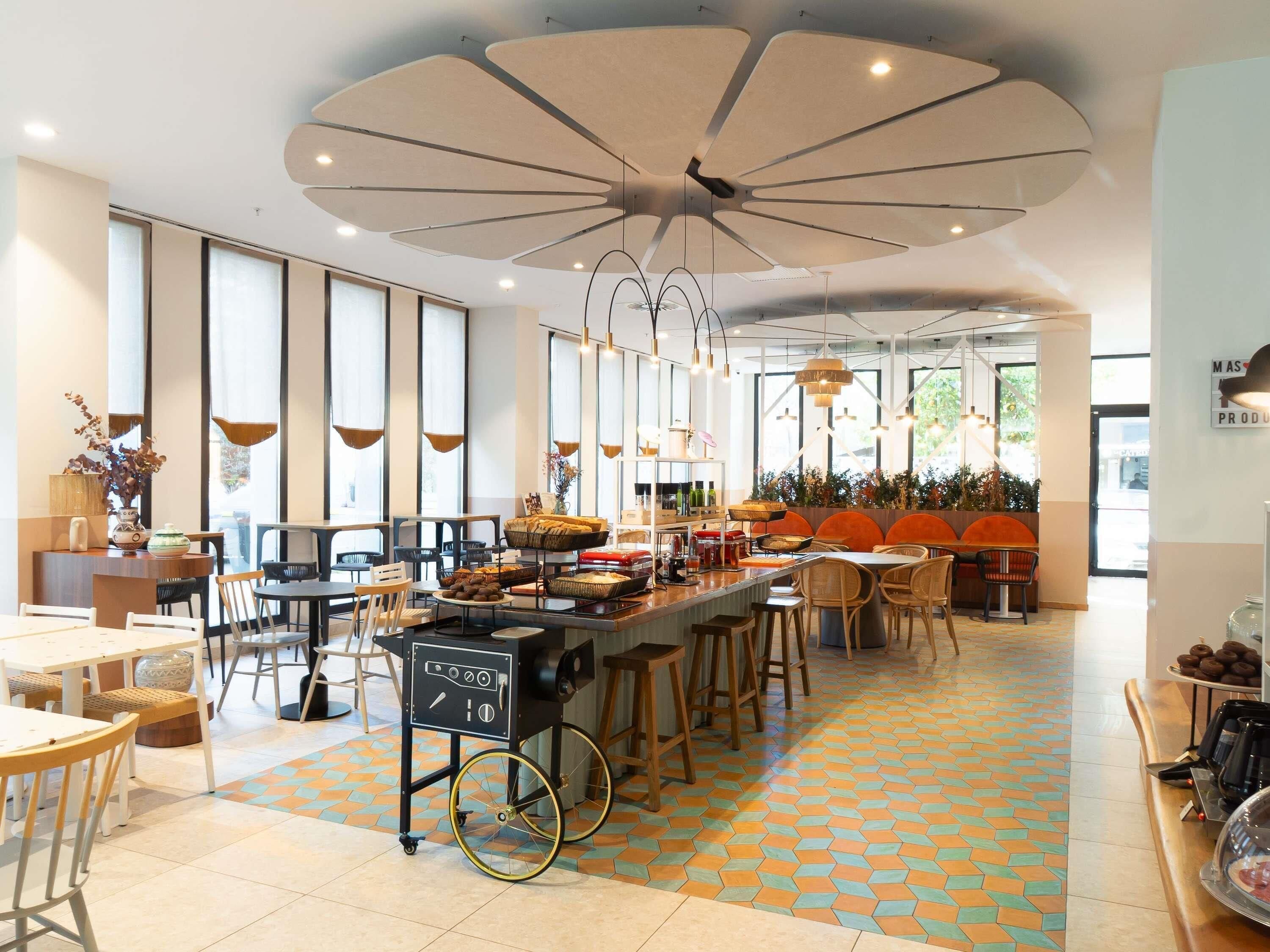 Una cafetería moderna con barra central, zona de estar y amplios ventanales.