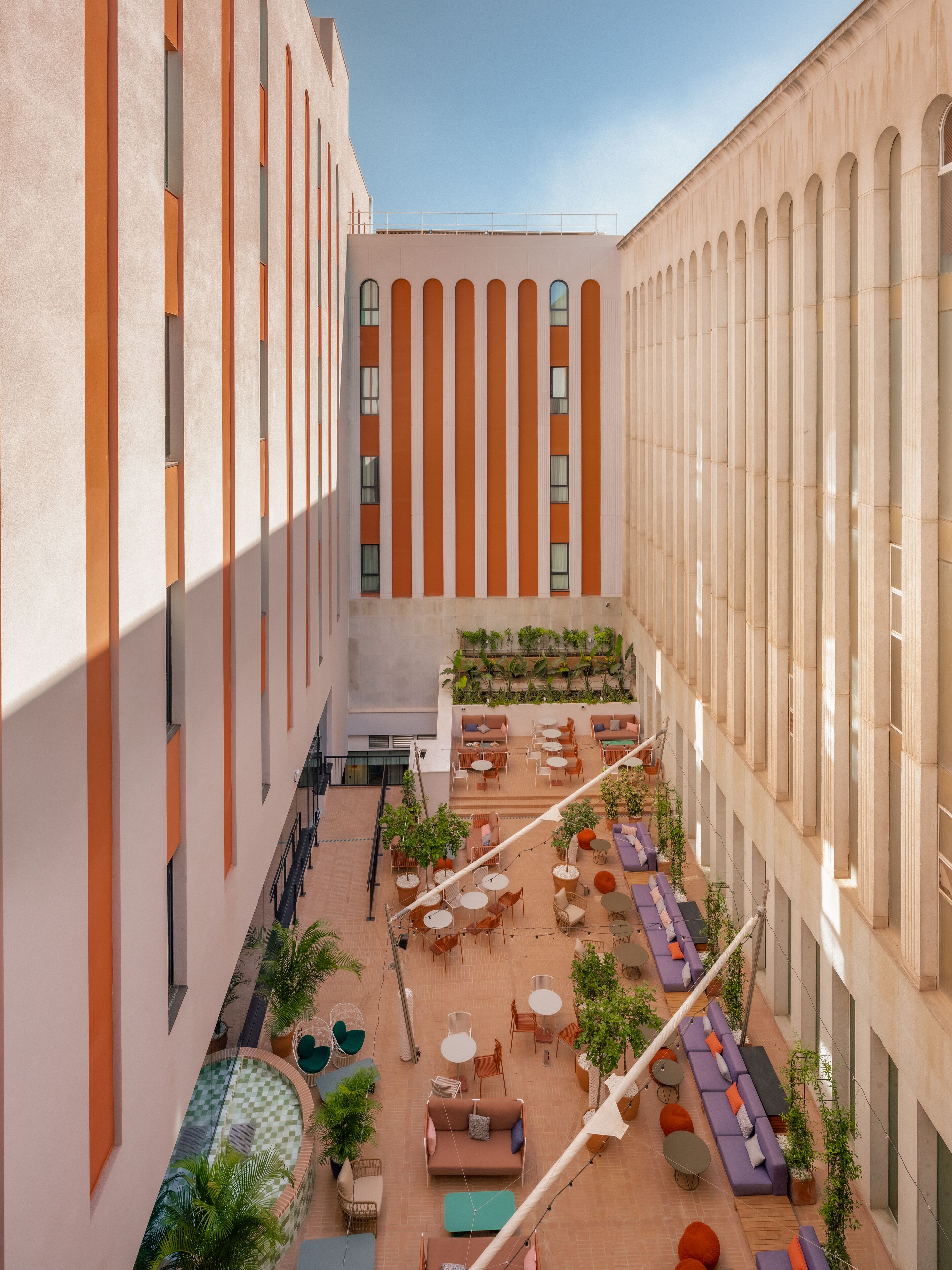 Une cour spacieuse avec des espaces de détente en plein air, une piscine et une vue sur l’architecture du bâtiment.