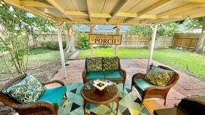 An outdoor patio with wicker furniture, a glass table, and a 'Welcome to the Porch' sign. - Super Cozy 4 Bedroom by Premier Host - Sleeps 10 |  (Katy)