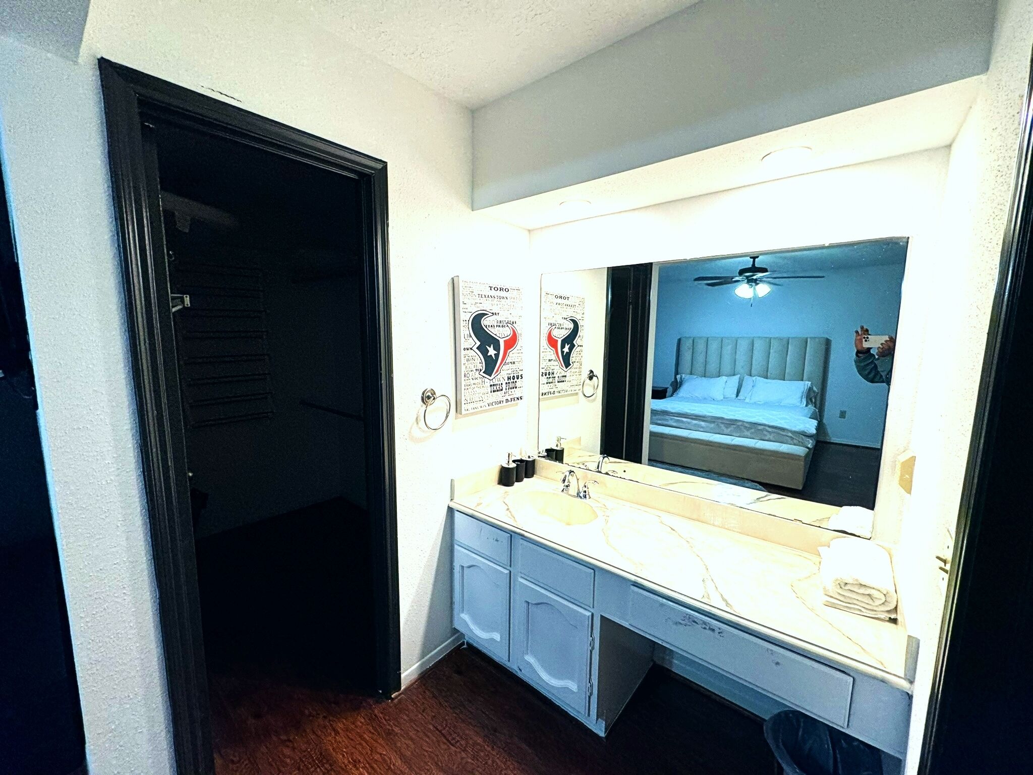 A hotel room with a large mirror, a bed with a headboard, a desk with a chair, and a door leading to another room.