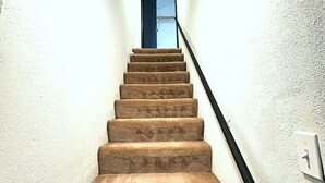 A carpeted staircase with a black handrail, white walls, and a ceiling light. - Super Cozy 4 Bedroom by Premier Host - Sleeps 10 |  (Katy)