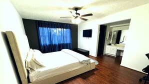 A bedroom with a bed, a ceiling fan, a window with curtains, a small desk, and a bathroom visible through an open door. - Super Cozy 4 Bedroom by Premier Host - Sleeps 10 |  (Katy)