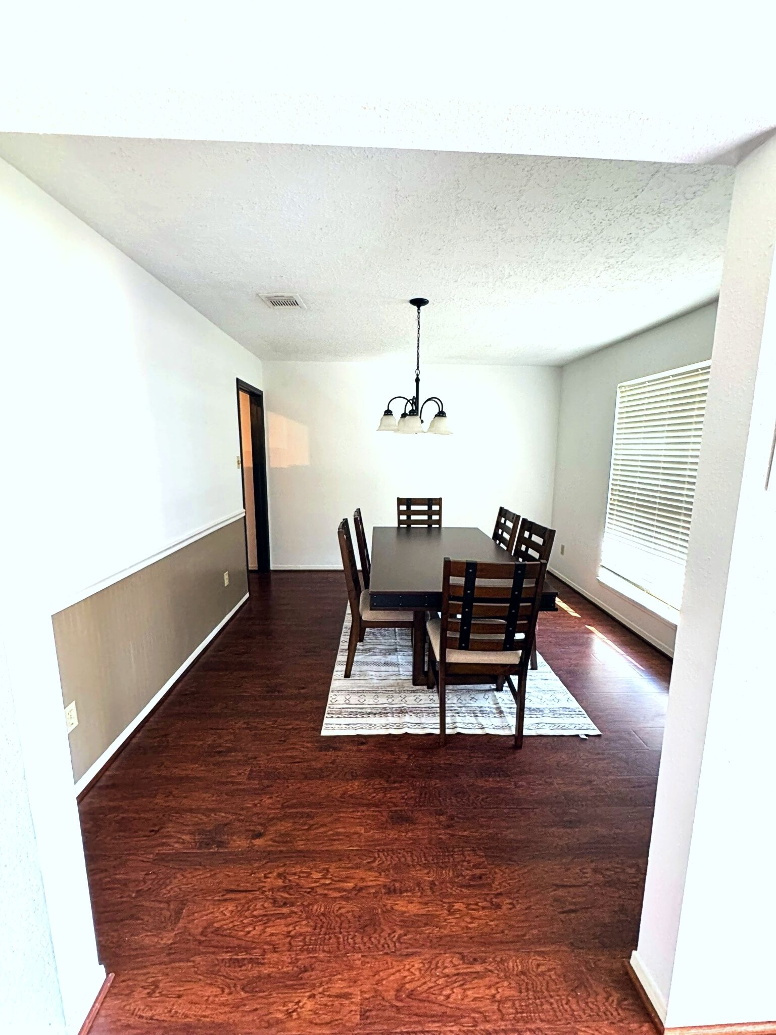 A dining area with a table and chairs, a chandelier, and a window with blinds.