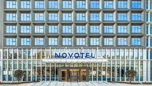 Een modern hotel met een raster van ramen, een glazen ingang en de naam 'NOVOTEL' boven de deuren.