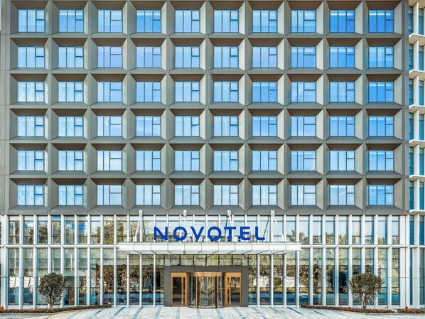 Ein modernes Hotel mit Rasterfenstern, einem Glastürbereich und der Aufschrift 'NOVOTEL' über der Eingangstür.