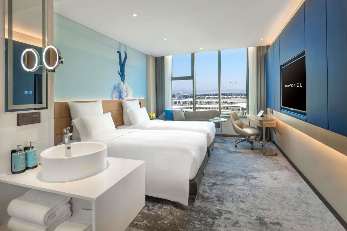 A hotel room with a large bed, a desk, a chair, a TV, and a bathroom with a sink and mirror.