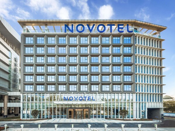 A modern hotel building with a prominent 'NOVOTEL' sign, large windows, and a structured facade. - Novotel Guangzhou Baiyun Airport (Guangzhou)
