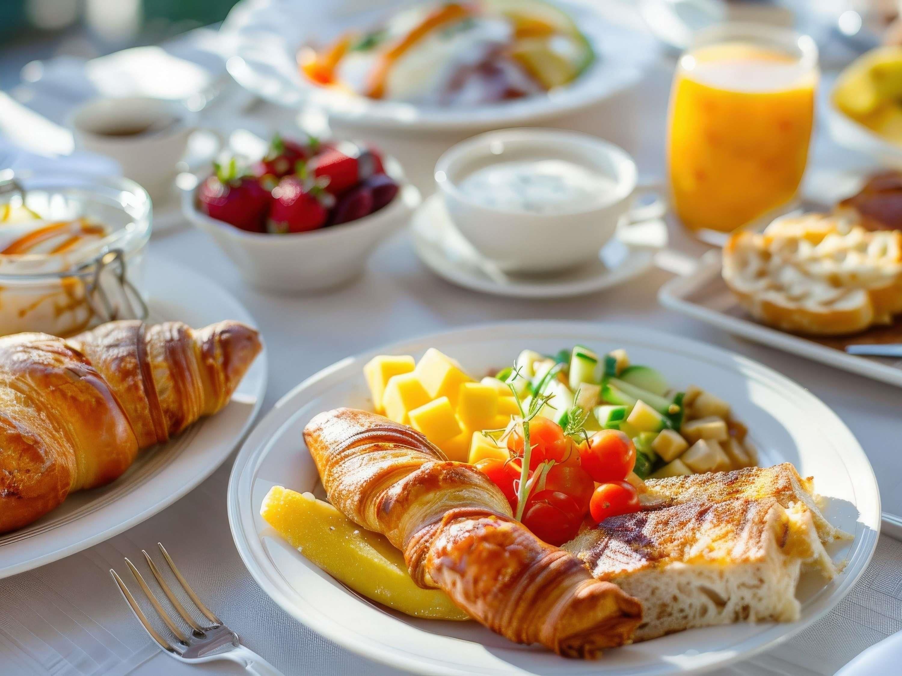 Une table dressée pour le petit-déjeuner avec des croissants, des fruits et un verre de jus d’orange.