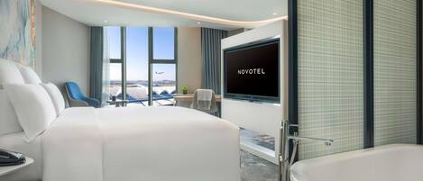 Une chambre d’hôtel moderne dotée d’un grand lit, d’une télévision, d’une baignoire et offrant une vue sur l’aéroport.