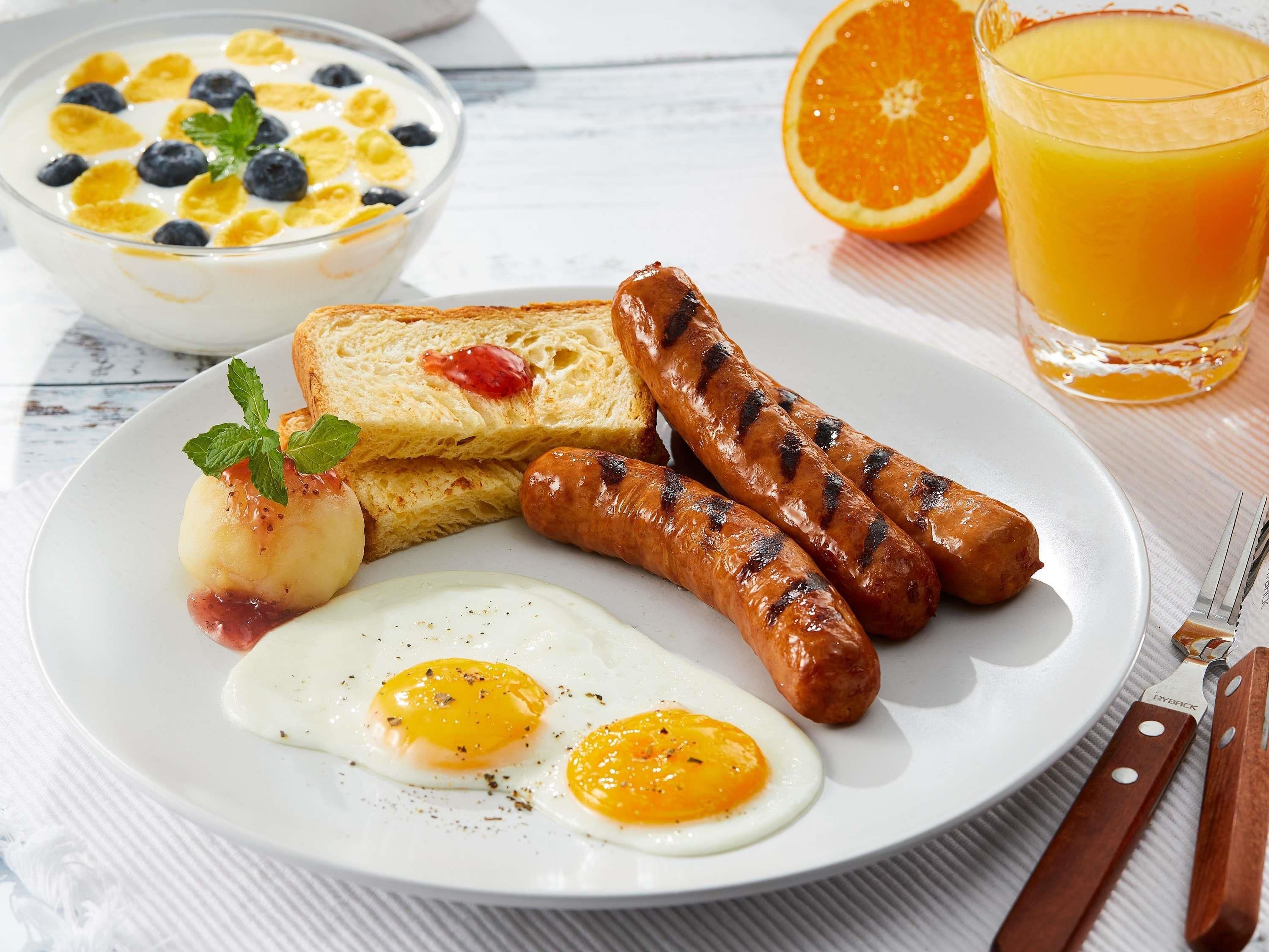 Un piatto per la colazione con salsicce, uova, pane tostato e una ciotola di cereali con frutta.