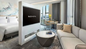 Une chambre d’hôtel moderne dotée d’une grande télévision à écran plat, d’un canapé, d’une table basse et d’un coin repas avec vue.