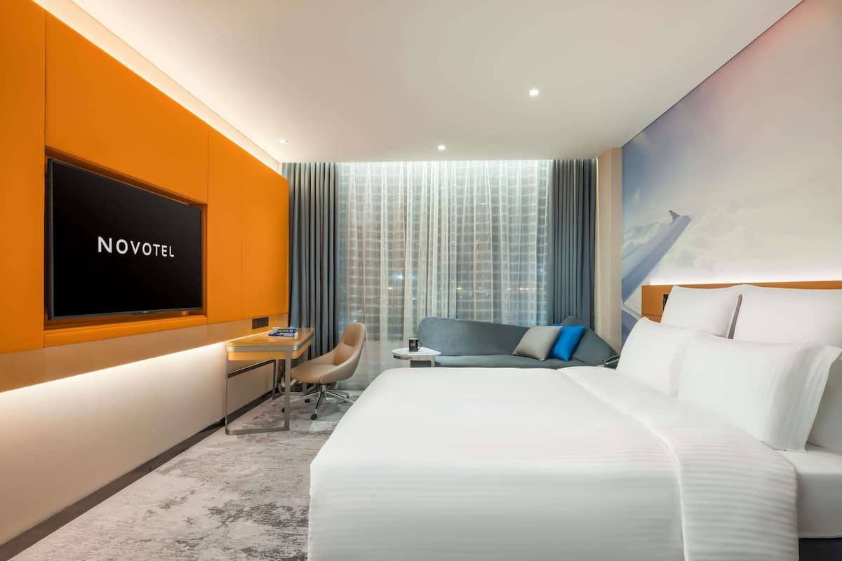 A hotel room with a bed, a desk, a chair, a TV, and a large window with curtains.