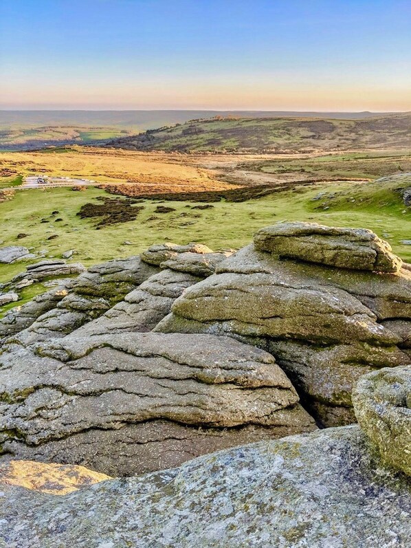 A rocky landscape with layered stone formations and a distant view of rolling hills.