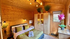 Un dormitorio de cabaña de madera con una cama, lámparas de noche, un armario y plantas en macetas.