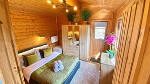 Un dormitorio acogedor tipo cabaña de madera con cama, mesitas de noche, un armario y una ventana pequeña.