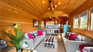 Interior acogedor de una cabaña con detalles de madera, un conjunto de sofás, un comedor y una cocina.