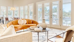 A spacious living room with a large sofa, a coffee table, and a dining area visible through glass doors. - Sunridge by AvantStay | Glorious Estate w/ Pool, Hot Tub, Ping Pong & Pool Table (Scottsdale)
