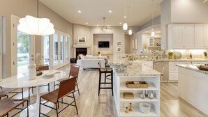 A spacious kitchen with a central island, a dining area with a round table and chairs, and a living area with a sofa and TV. - Sunridge by AvantStay | Glorious Estate w/ Pool, Hot Tub, Ping Pong & Pool Table (Scottsdale)