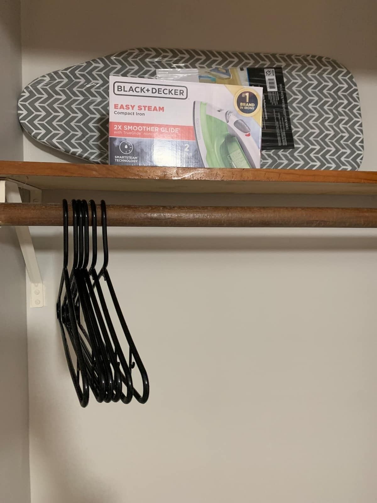 Un paquete de plancha compacta Easy Steam de BLACK+DECKER sobre una estante, con una tabla de planchar estampada debajo.