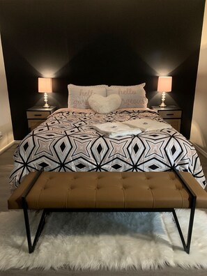Une chambre à coucher avec une couvre-lit à motifs, deux lampes de chevet, un coussin en forme de cœur et un banc.