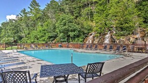 A swimming pool with lounge chairs and a table, surrounded by a wooden fence and lush greenery. - Cozy Mountain Retreat, Open Concept, 7 Min To GSM Parkway, 5Br/5Ba, King Beds, (Sevierville)