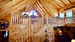 A wooden cabin interior with a staircase, wooden railings, a chandelier, and a window with a view of trees. - Cozy Mountain Retreat, Open Concept, 7 Min To GSM Parkway, 5Br/5Ba, King Beds, (Sevierville)