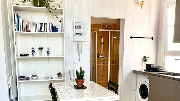 A compact kitchen with a dining area, a built-in bookshelf, and a washing machine.