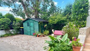 A garden with a green shed, potted plants, and a red bench.