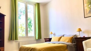 A bedroom with a bed, two bedside lamps, a window with green curtains, and a small rug on the floor.