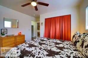 Ein Schlafzimmer mit einem Bett, einem Deckenventilator, einem Schminktisch, einem Spiegel und einem roten Vorhang.
