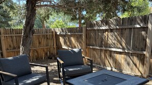 Een terras met twee stoelen en een vierkante tafel, omringd door een houten hek en bomen.