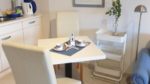 Una cocina moderna con armarios blancos, una mesa de comedor con sillas, una cafetera y un cuadro en la pared.