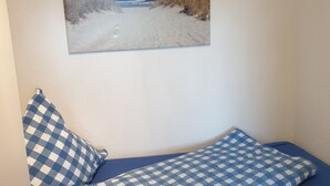 Una cama con una colcha azul y blanca a cuadros, un almohadón a juego y un cuadro de una playa en la pared de arriba.