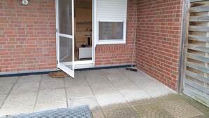 Una habitación con pared de ladrillo, ventana con persianas, una puerta y una pequeña mesa con una silla.