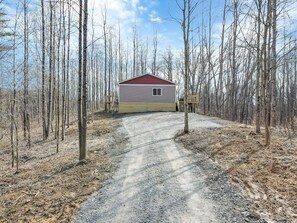 A single-story cabin with a red roof, surrounded by a forest of leafless trees. - Deerberry Ridge (Hocking Hills Area) (Rockbridge)