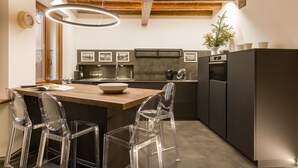 Una cocina moderna con una isla de madera, sillas transparentes y una lámpara colgante.