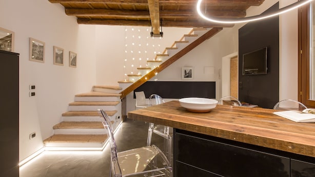 Una cocina moderna con encimera de madera, sillas transparentes y una escalera con escalones de madera.