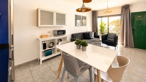 A modern kitchen with a dining table, chairs, and a microwave. There is a sofa and a green door in the background. - Appartement Villalia  (Puerto del Carmen)