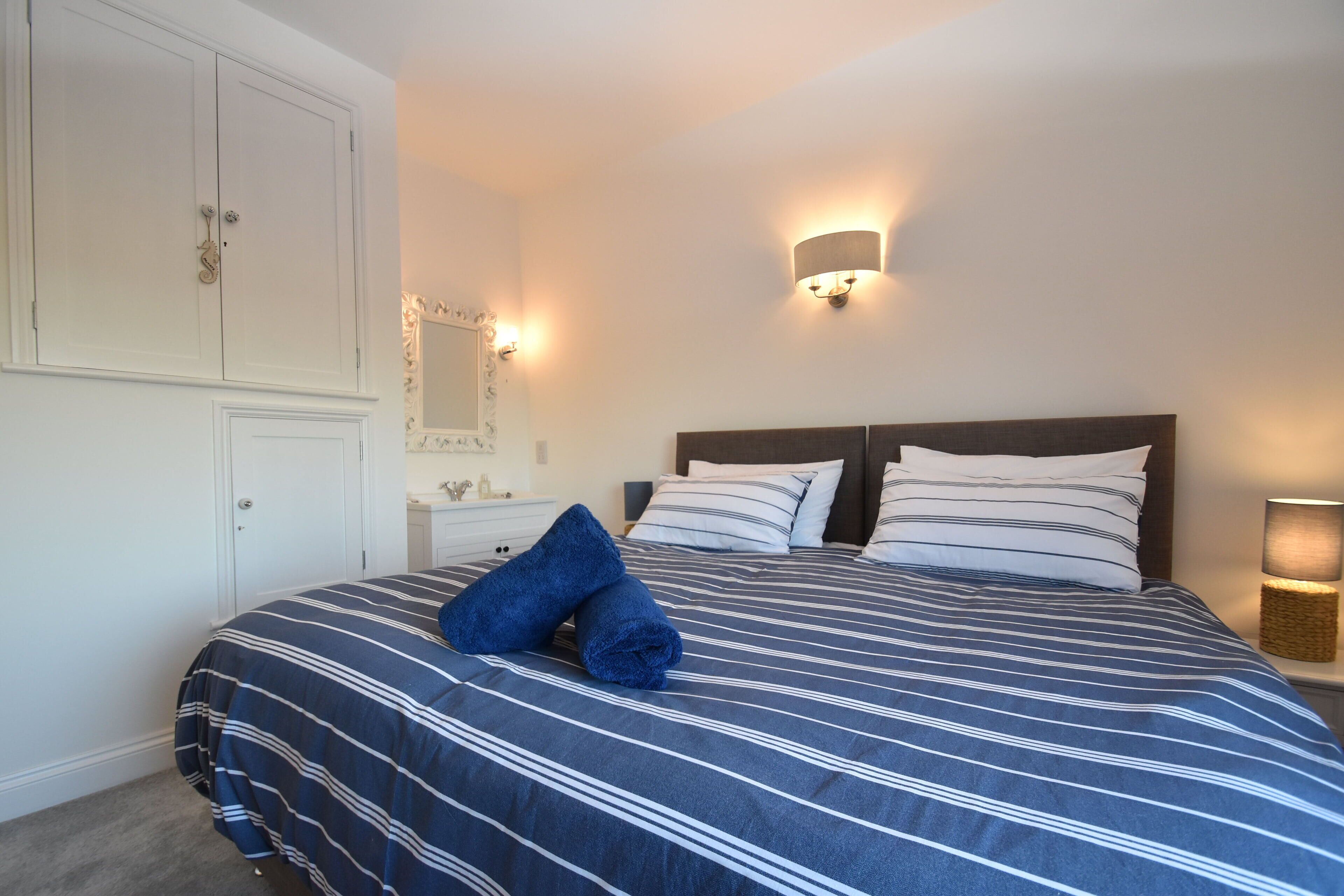 A bedroom with a large bed, a wardrobe, a mirror, and a wall-mounted light fixture.