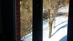 A window with a view of a snowy landscape, including trees and a brick wall. - L'ETERLOU in a charming property in the heart of the Source-Bleue area (Montperreux)