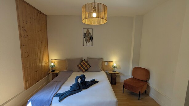 A hotel room with a bed, two bedside lamps, a wooden headboard, a wall-mounted artwork, and a brown armchair.