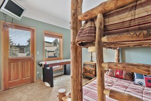 A rustic bedroom with a bunk bed, a wooden desk, and a television mounted on the wall.
