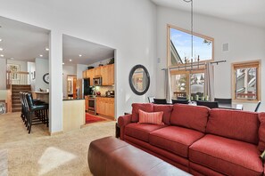 A spacious living area with a red sofa, a kitchen in the background, and a large window providing natural light.