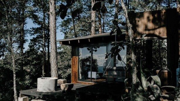 A modern cabin with a wooden deck, a fireplace, and a large window overlooking a forested area. - Cabañas Rancho Viejo (San Mateo Río Hondo)