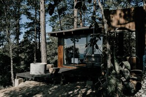 A modern cabin with a wooden deck, a fireplace, and a large window overlooking a forested area. - Cabañas Rancho Viejo (San Mateo Río Hondo)