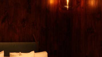 A bed with white bedding and a patterned blanket, set against a wooden wall with a hanging light fixture.