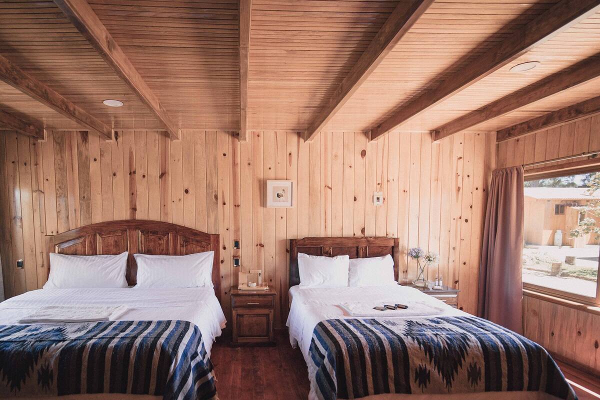 Une chambre de chalet en bois avec deux lits, chacun doté d’une tête de lit en bois et de linge de lit blanc.