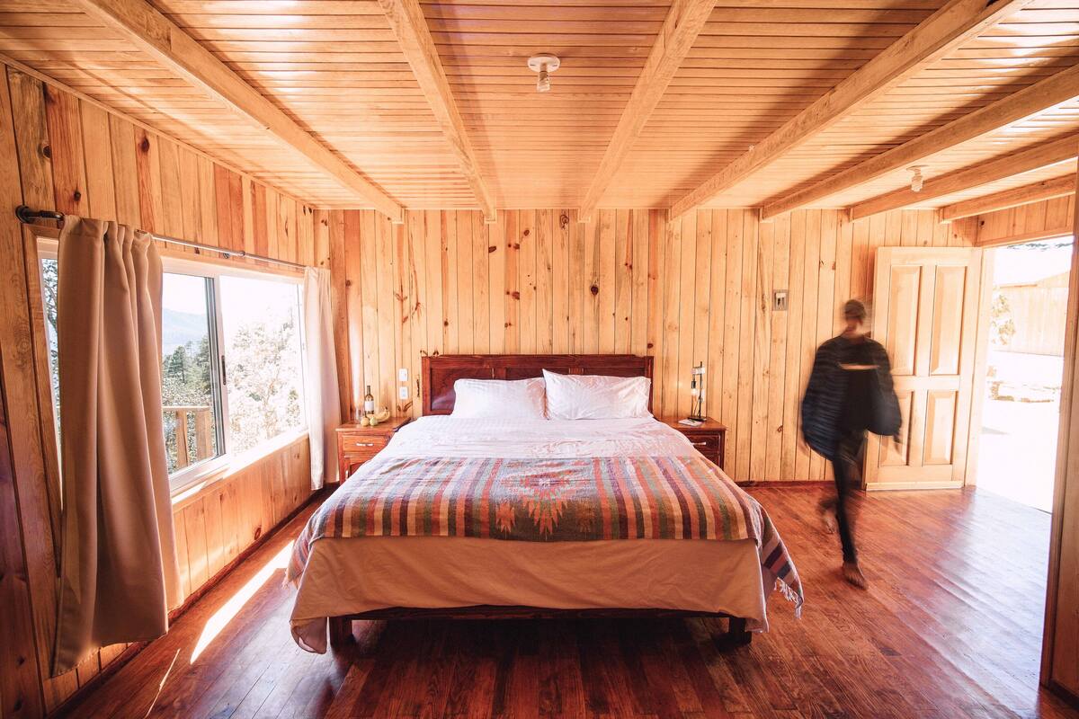 Une chambre dans une cabane en bois, avec un grand lit, des murs en bois et une fenêtre avec des rideaux.