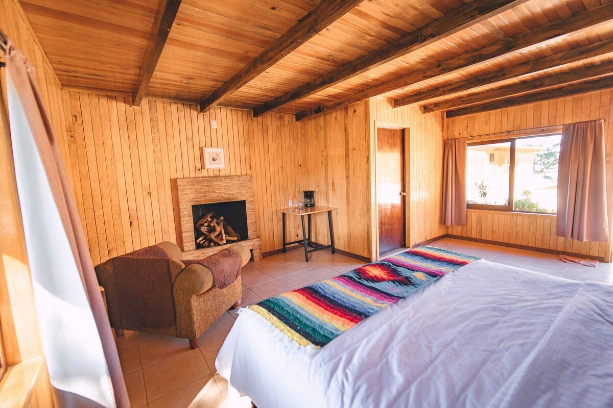 Une pièce de style cabane en bois, comprenant un lit, une chaise, une cheminée et une fenêtre.