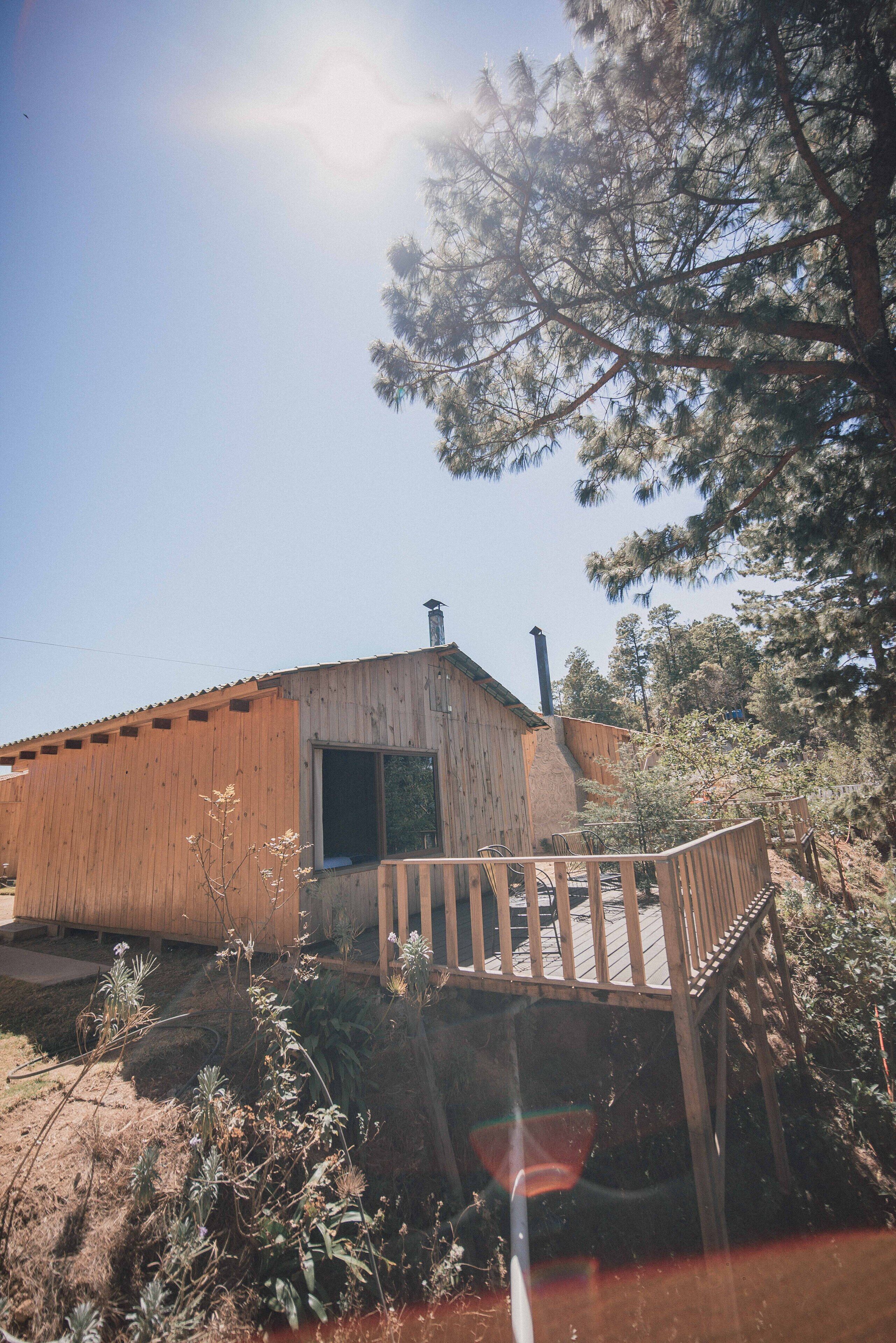 A wooden cabin with a chimney, a deck, and a large window.